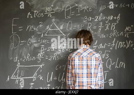 Ragazzo Teenageer problemi con complicate formule matematiche sulla lavagna nera Foto Stock