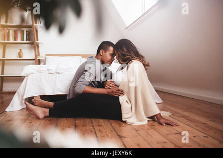Romantica giovane coppia seduta sul pavimento. Uomo e donna in attesa di un bambino. donna incinta con marito che si rilassa a casa, tenendo le mani sulla pancia. Foto Stock