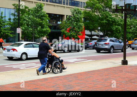 L'uomo spingendo la persona in sedia a rotelle su un ampio marciapiede vicino al Porto Interno di Baltimore, Maryland, Stati Uniti d'America Foto Stock