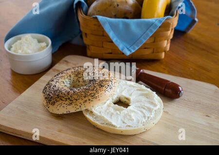 Semi di papavero bagel con formaggio cremoso con un paniere di assortimento di bagel in background. Foto Stock