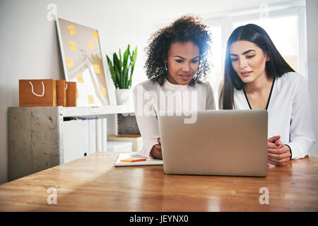 Due solerti donne giovani colleghi di lavoro seduta la condivisione di un computer portatile che lavorano insieme a loro small business in un concetto di entrepreneurshi Foto Stock