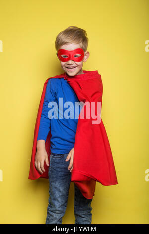 Ragazzo in rosso super hero cape e maschera. Superman. Ritratto in studio su sfondo giallo Foto Stock