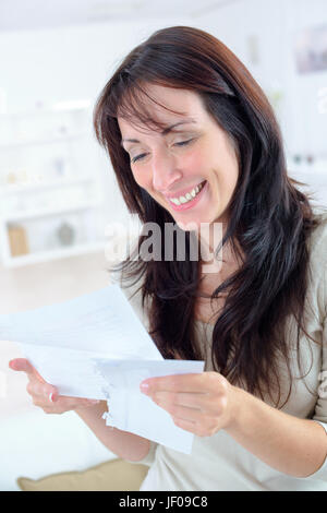 Excited donna informale la lettura di buone notizie in una lettera Foto Stock