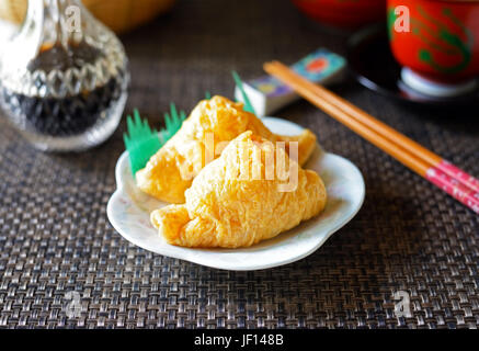 Un primo piano di giapponese inarizushi (inari sushi) su un piatto bianco contro uno sfondo scuro. Foto Stock