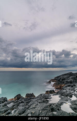 Spessa e pesante flottante nuvole sopra il mare e la costa rocciosa in Padangbai, Indonesia. Foto Stock