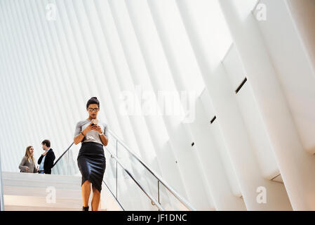 Una donna che cammina giù per una scalinata all'occhio dell'edificio, il World Trade Center hub, design architettonico moderno con un soffitto a volta nervata spazio sul tetto. Foto Stock