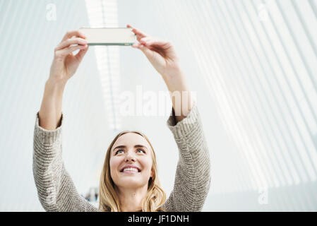 Una giovane donna di scattare una fotografia con il suo cellulare un selfy nel World Trade Center Oculus edificio con una splendida striata di bianco tetto ad arco. Foto Stock