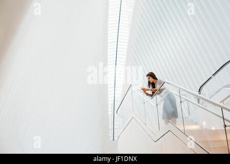 Una donna su per le scale appoggiate su di una ringhiera nel vasto spazio dell'atrio dell'occhio edificio al sito del World Trade Center a New York City. Foto Stock