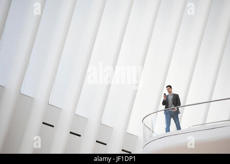 Una persona in piedi da solo in un atrio da una ringhiera, sotto un alto bianco soffitto rigata. Foto Stock