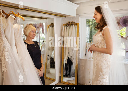 Una donna, una sposa per essere, cercando su vestiti con l'aiuto di un assistente alle vendite in un abito da sposa shop. Foto Stock