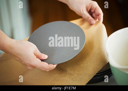 Chiudere fino ad alto angolo di visione della persona in possesso di rotondo di metallo teglia la base sopra la carta da forno. Foto Stock