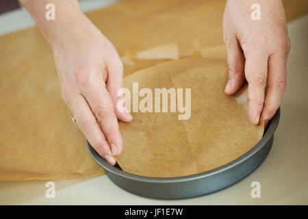 Chiudere fino ad alto angolo di visione della persona il rivestimento inferiore di un round in una teglia con carta da forno. Foto Stock