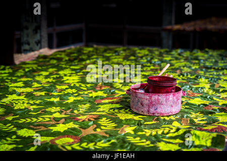 Un colorato di verde e giallo pezzo di mano-cerata batik indonesiani posa sopra il tavolo di lavoro con pochi strumenti di lavoro sulla parte superiore. Foto Stock