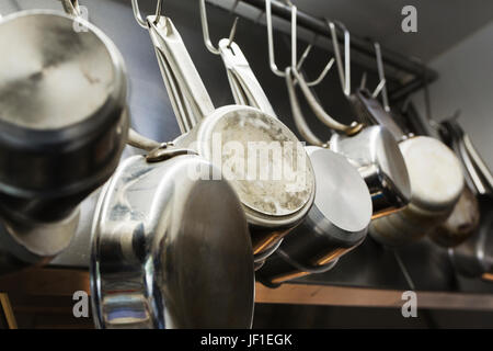 Chiudere fino in acciaio inossidabile di pentole e tegami appesi a ganci di metallo su un ripiano in un ristorante di cucina. Foto Stock