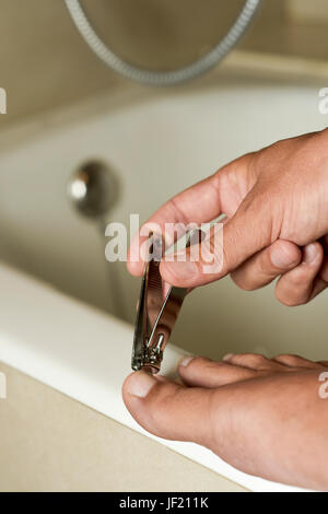 Primo piano di un giovane uomo caucasico in bagno il suo taglio toenails con un tagliaunghie Foto Stock