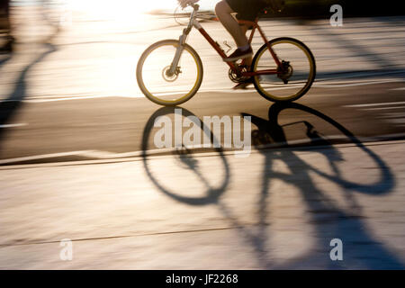 Sfocata ciclista silhouette e ombra su un percorso in bicicletta nel tramonto, panning shot Foto Stock