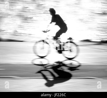 Ciclista sfocati silhouette e ombra su di una pista ciclabile lungo il fiume con acqua la riflessione in bianco e nero a contrasto elevato Foto Stock