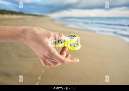 Mano femmina giallo holding agitano: spinner su sfondo sfocato di Ocean Beach Foto Stock