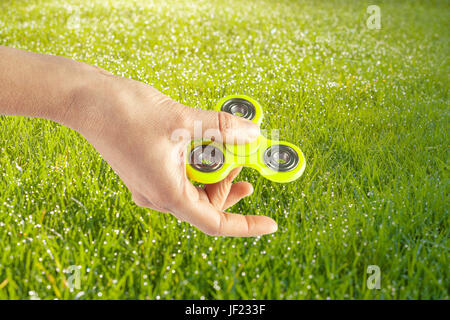 Mano femmina giallo holding agitano: spinner su un prato sfondo soleggiato Foto Stock