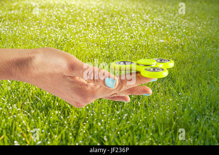 Mano femmina giallo holding agitano: spinner su un prato sfondo soleggiato Foto Stock