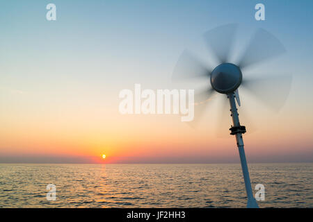 Marine turbina a vento sulla barca a vela con lame di rotazione utilizzando il potere di vento per caricare le batterie di bordo sul Mare del Nord al tramonto, Paesi Bassi Foto Stock
