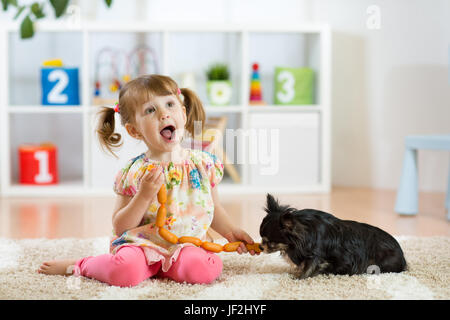 Bambino ragazza salsicce di alimentazione per il suo cane sul pavimento in vivaio Foto Stock