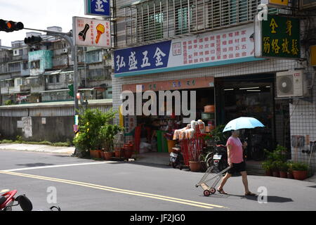 Vecchia donna tirando cestello dietro di lei in strada vicino a memorizzare nella nuova città di Taipei. Caldo giorno d'estate. Foto Stock