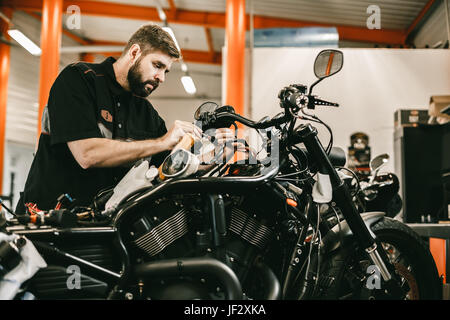 Uomo che ripara electronics nero sport bike. Fiducioso giovane uomo che ripara moto nel negozio di riparazione. Foto Stock