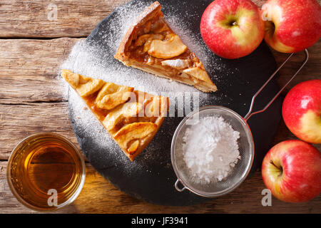 Tagliare appena sfornato la torta di mele con lo zucchero in polvere di close-up sul tavolo. vista orizzontale dal di sopra Foto Stock