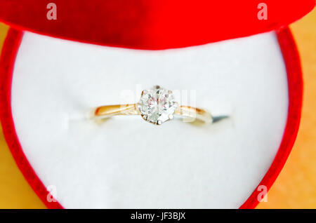 Close up (macro) di oro e diamante solitario anello di fidanzamento, ripresa dall'alto, in un aperto cuore rosso scatola sagomata con interno bianco. Foto Stock