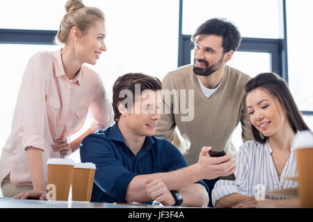 Un gruppo di giovani uomini di affari che utilizza lo smartphone su piccole riunioni aziendali Foto Stock