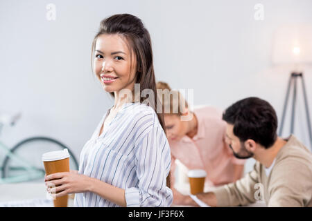 Ritratto di sorridere imprenditrice azienda tazza da caffè con i colleghi nelle vicinanze Foto Stock