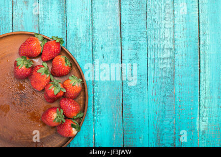 Rosso fresco Fragole in piastra ceramica sul turchese da tavolo in legno, bacche sul concetto di legno Foto Stock