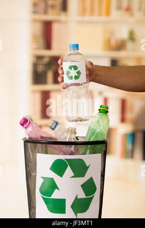 In prossimità di un lato mettendo una bottiglia di plastica all'interno di un piccolo nero garbage collector piena di plastica, con un segno di riciclaggio stampato nella parte anteriore, riciclare Foto Stock