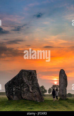 Una giovane coppia guardare il sole sorgere sopra le antiche pietre Sarsen ad Avebury nel Wiltshire all alba del giorno prima del Solstizio d'estate. Foto Stock