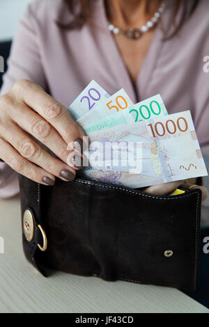 Donna mettendo Swedish kronas nel suo portafoglio Foto Stock