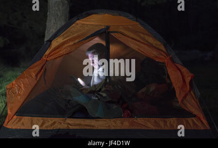 L'uomo guarda il suo smartphone in una tenda. Foto Stock