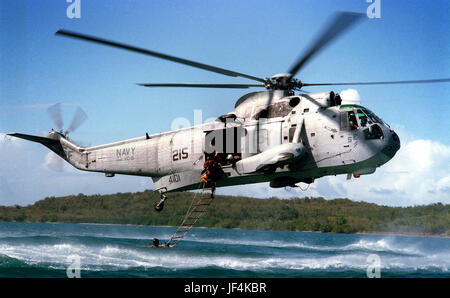 Un U.S. Navy SH-3H Sea King elicottero si libra sopra l'acqua a recuperare l'eliminazione degli ordigni esplosivi tecnici salendo una scala per l'aeromobile. DoD foto di Sottufficiali di prima classe Michael Rinaldi, U.S. Navy Foto Stock