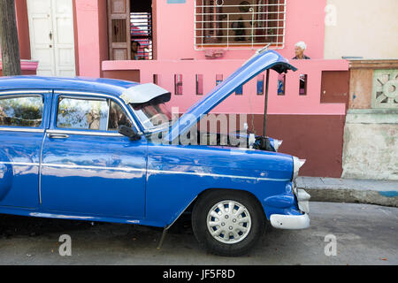 Per le strade del centro di Havana, il cofano di un classico americano auto viene sollevato per la manutenzione mentre persone sedersi intorno a casa loro. Foto Stock