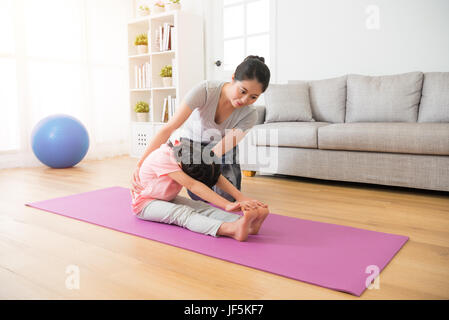 Lo yoga coach ginocchio all insegnamento i bambini seduti sul pavimento in legno con mat come relax facendo stretching azione di ginnastica in palestra personale ce Foto Stock