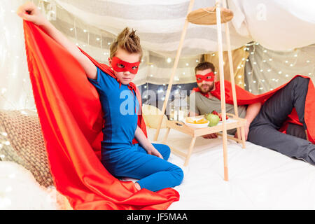 Padre e figlio in costumi di supereroi per divertirsi insieme in una coperta fort Foto Stock