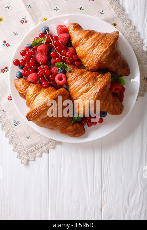 Croissant appena sfornati con lamponi, mirtilli e ribes close-up su una piastra. vista verticale da sopra Foto Stock