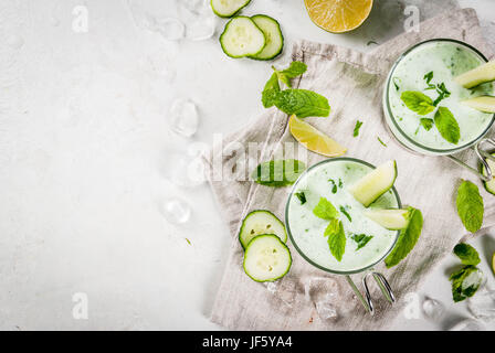 Estate cibo. Piatti rinfrescanti. Zuppa fredda di cetriolo, avocado, con le erbe e le foglie di menta. Con bicchieri di servizio, con fette di cetriolo. Su un cemento bianco Foto Stock