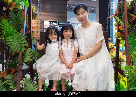 Asian madre cinese e le figlie seduto su una swing sul giardino interno Foto Stock