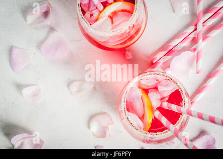 Estate bevande ristoro. Luce rosa rosa cocktail con vino rosato, tè petali di rosa, limone. Su una pietra bianca tabella di calcestruzzo. Con strisce di tubuli rosa Foto Stock