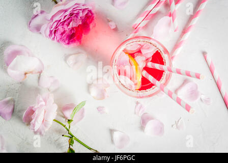 Estate bevande ristoro. Luce rosa rosa cocktail con vino rosato, tè petali di rosa, limone. Su una pietra bianca tabella di calcestruzzo. Con strisce di tubuli rosa Foto Stock