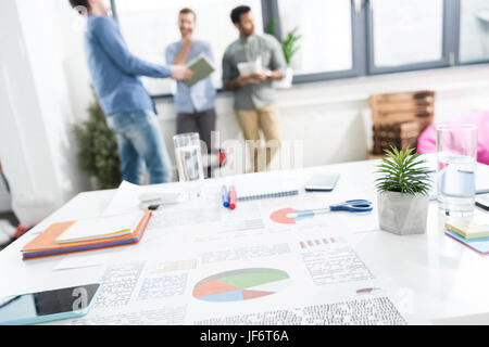 Vista ravvicinata di documenti e grafici aziendali sulla scrivania e di imprenditori in piedi dietro, business concetto del lavoro di squadra Foto Stock