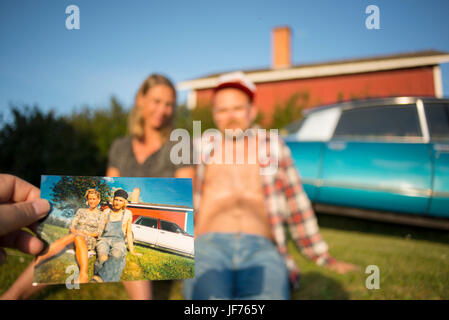 La gente seduta davanti a casa con la persona che tiene la foto in primo piano Foto Stock