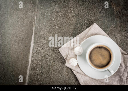 Pausa caffè. La prima colazione. Mattina. Tazza di caffè e due meringhe su di una pietra scura tabella. Vista dall'alto uno spazio di copia Foto Stock