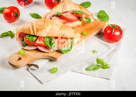 Luce e sostanziosa colazione a molla. Croissant con prosciutto e formaggio e pomodoro fresco e basilico. Su una pietra bianca, tavola con gli ingredienti. Spazio di copia Foto Stock